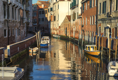 Venetian city landscape at sunset. Moored boats along the canal shore.