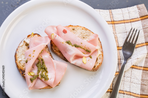 Close up of mortadella toast with tomatoes on a white plate