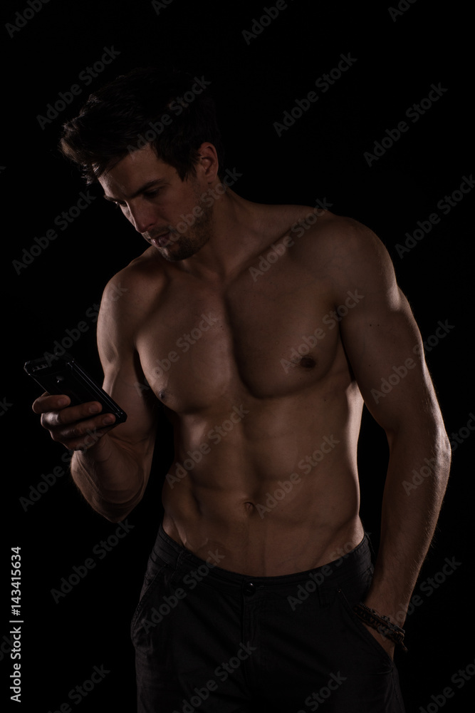 Handsome shirtless muscular young man using cell phone