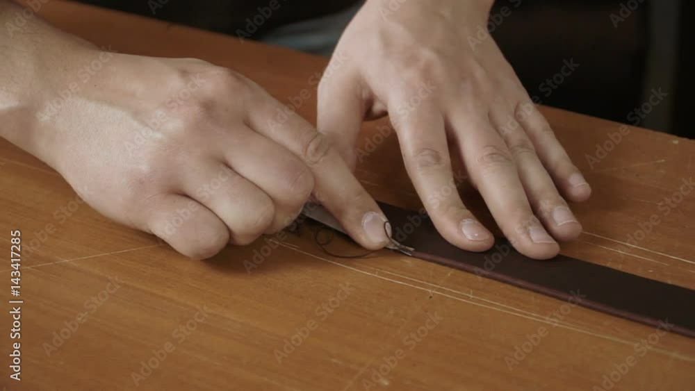 Close up view of craftsman's hands working with a piece of leather on the table. Making a leather handbag.
Close up view of craftsman's hands working with a piece of leather on the table. Making a leather handbag.