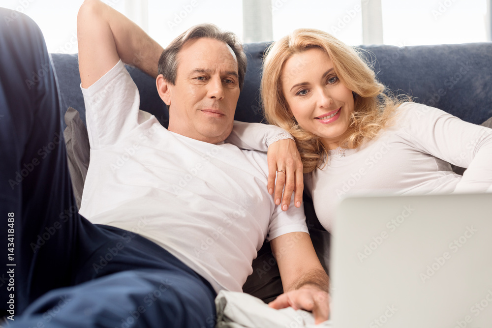 Happy middle aged couple using laptop and lying on bed at home Happy middle aged couple using laptop and lying on bed at home