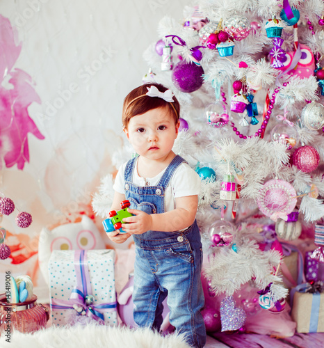 Girl in jeans jumpers plays before pink and white Christmas tree