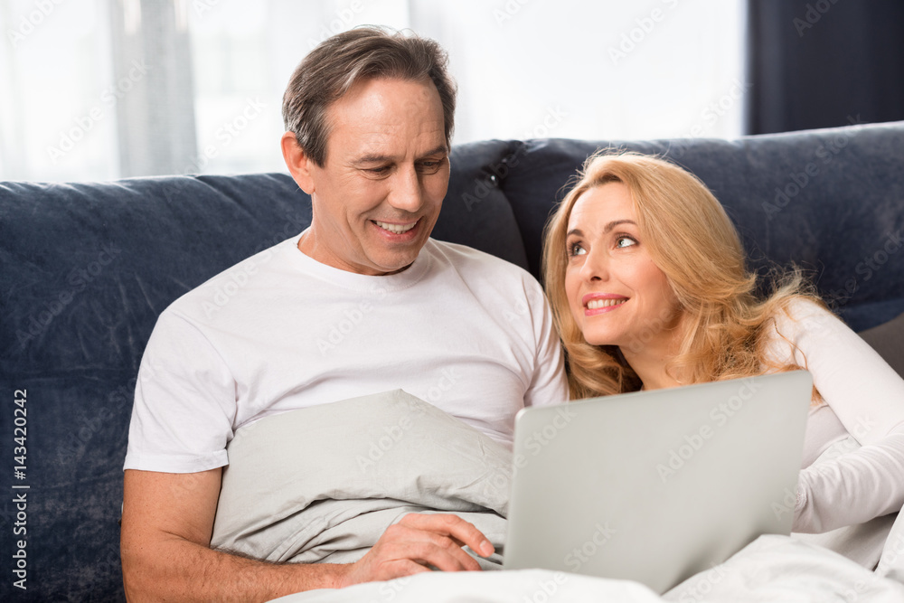 Happy middle aged couple using laptop and lying on bed at home Happy middle aged couple using laptop and lying on bed at home