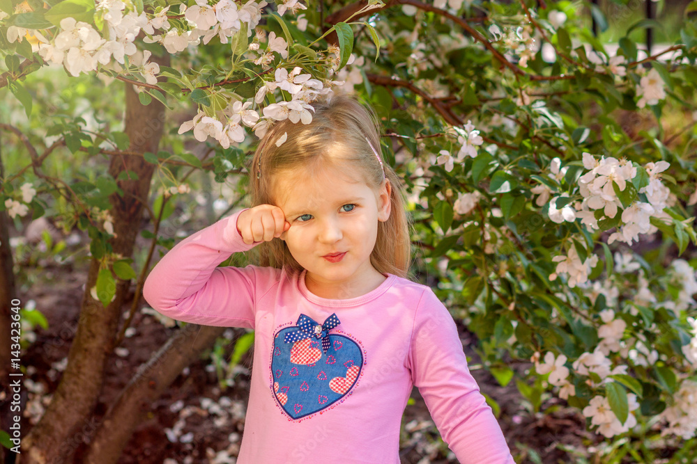 Portrait of a girl in flowers. A blonde girl in a pink dress with a heart is near of the branches of a blossoming Apple tree. Spring portrait of a child Portrait of a girl in flowers. A blonde girl in a pink dress with a heart is near of the branches of a blossoming Apple tree. Spring portrait of a child