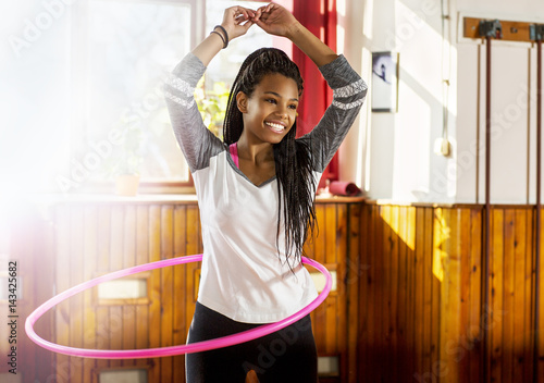 Beautiful young girl in a gym.
Cute African girl on a training. She’s spinning a hula hoop. Indoors.