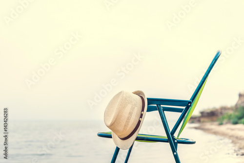 Summer straw hat hanging on a folding chair on the background of the sea. Sunrise on the sea. Travels