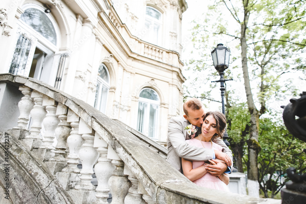 Groom hugs bride from behind standing on stone stairs of an old house