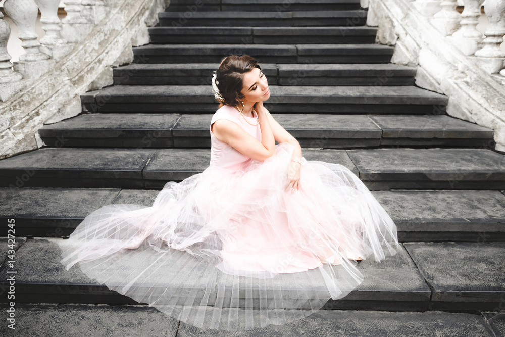 Bride in light summer dress sits on the stone stairs Bride in light summer dress sits on the stone stairs