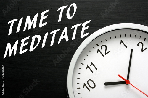 The words Time to Meditate written on a blackboard next to a modern wall clock as a reminder to set aside time for meditation and relaxation