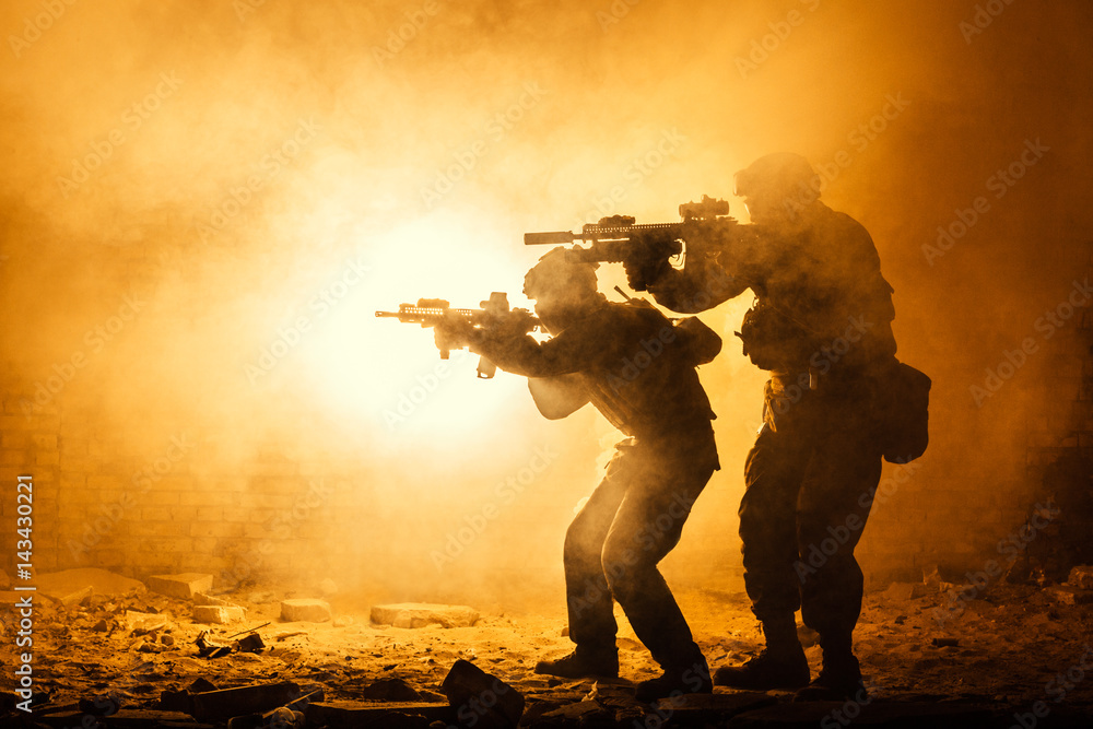 Φωτογραφία Black silhouettes of pair of soldiers in the smoke fire burning moving in battle operation