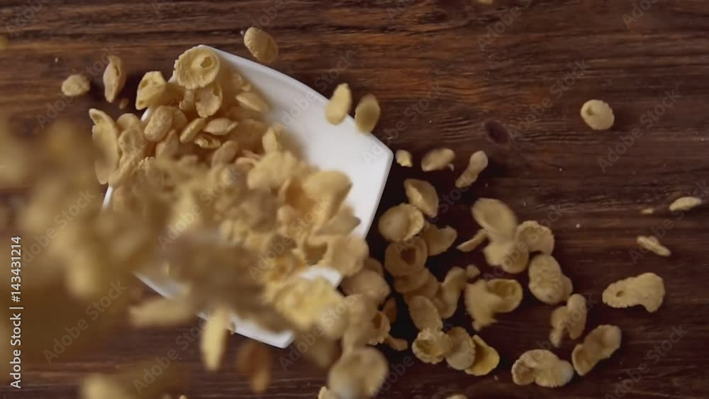 Corn flakes falling in white bowl with copyspace to the right on wooden table Corn flakes falling in white bowl with copyspace to the right on wooden table