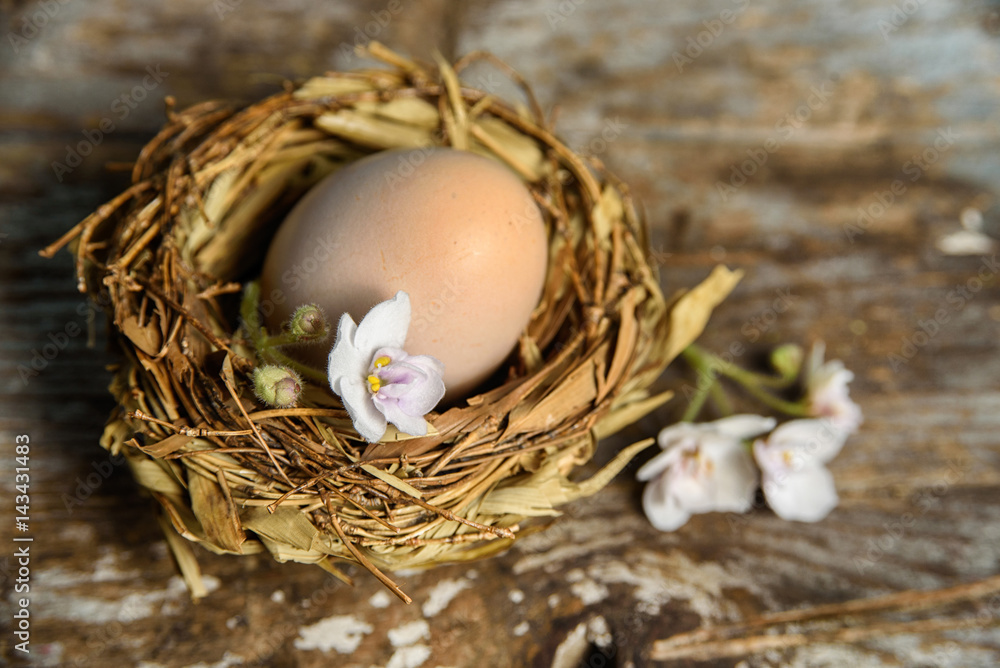 Rustic easter background with easter egg in a nest and flowers on vintage wooden table