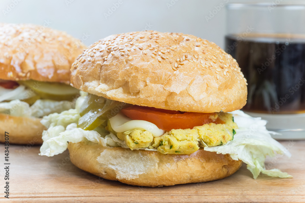 Vegetarian burgers on wood cutting board. Close-up image of vegetarian hamburgers on natural table with glass of soft cola drink in background Vegetarian burgers on wood cutting board. Close-up image of vegetarian hamburgers on natural table with glass of soft cola drink in background