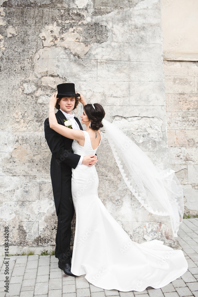 Beautiful bride hugs tall groom in black tuxedo and topper Beautiful bride hugs tall groom in black tuxedo and topper
