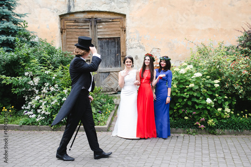 Cuadro en lienzo Man in tailcoat and topper passes bride and bridesmaids standing on the road