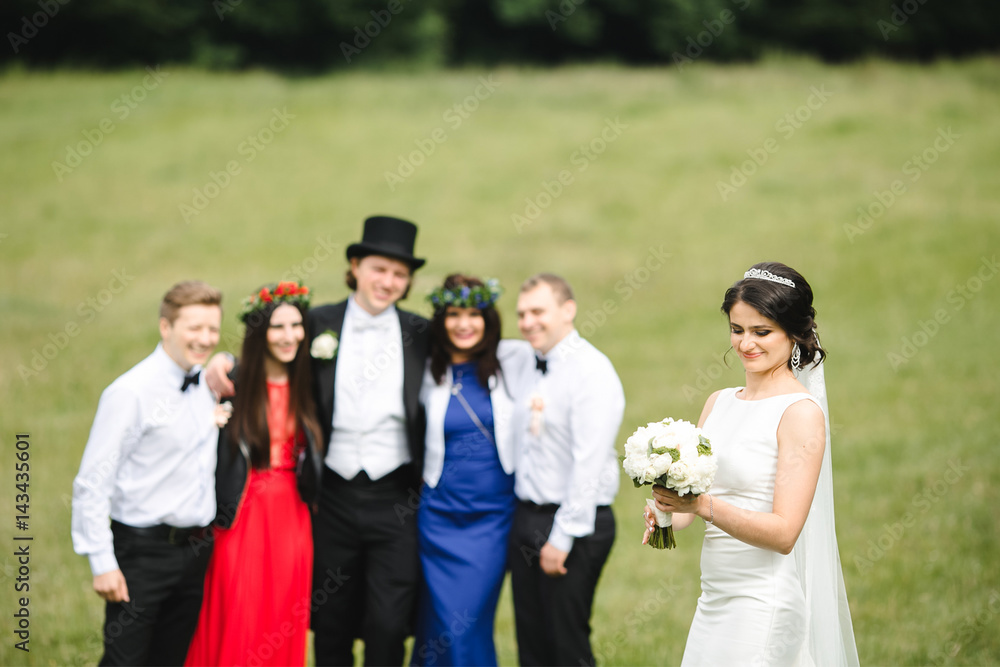 Tall groom in topper and tailcoat stands with friends and looks at pretty bride Tall groom in topper and tailcoat stands with friends and looks at pretty bride