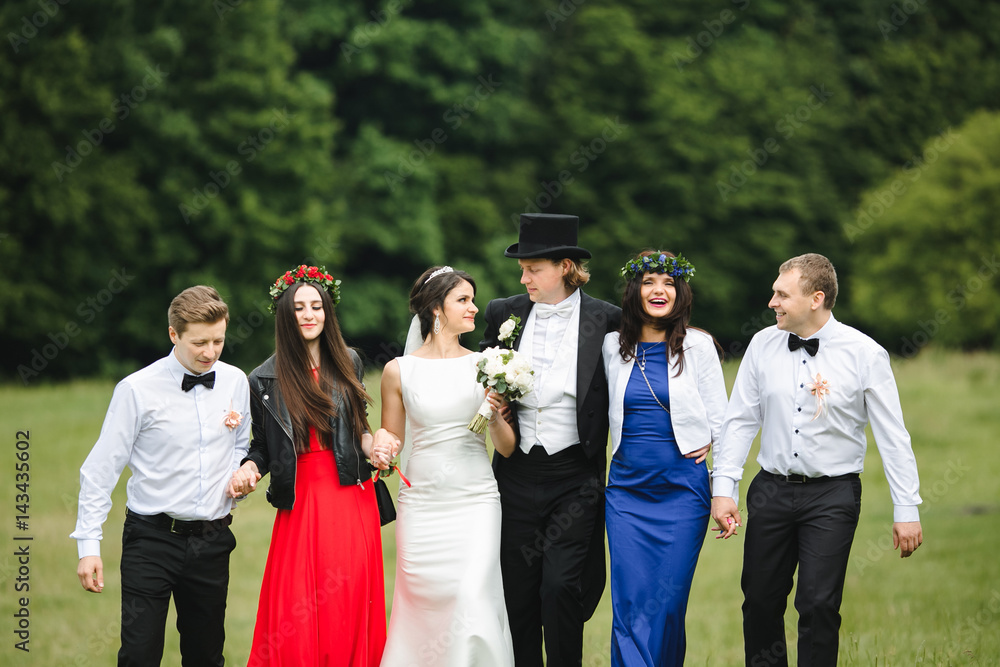 Φωτογραφία Newlyweds and their friends in colorful closes walk across the lawn