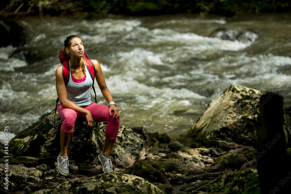 Young woman hiker rests next to the forest river Young woman hiker rests next to the forest river