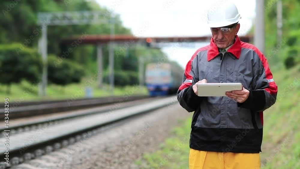 Railway employee with tablet computer on railway line. Inspector of railway traffic makes notes in his tablet computer. Railway worker with tablet pc in hands looks at the train Railway employee with tablet computer on railway line. Inspector of railway traffic makes notes in his tablet computer. Railway worker with tablet pc in hands looks at the train