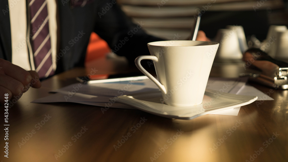 Eine Tasse Tee steht auf dem Tisch, während ein Geschäftsmann seine Anlagepapiere liest Eine Tasse Tee steht auf dem Tisch, während ein Geschäftsmann seine Anlagepapiere liest