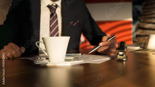Kaffeetasse steht auf einem Schreibtisch während ein Unternehmer Verkaufszahlen prüft