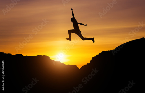 Silhouette of athlete, jumping over rocks in mountain area against sunset. Training running and jumping in difficult conditions in a beautiful nature with cloudy sky