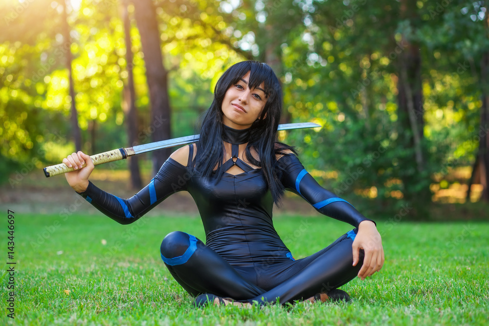Young girl sitting on the grass and holding samurai sword. Original cosplay character
