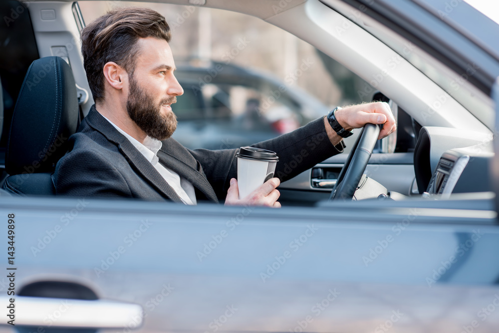 Handsome businessman driving a car with coffee to go in the city