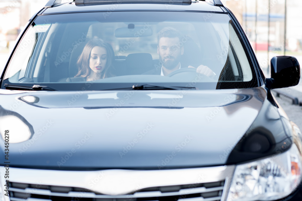 Business couple having a conversation while driving a car. Front view through the windshield