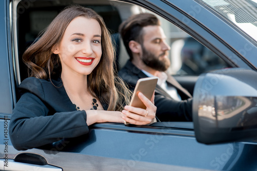 Portrait of a beautiful businesswoman sitting in the car with businessman driver