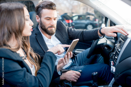 Businesswoman showing phone to the businessman sitting together on the front in the car
