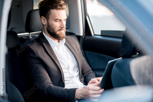 Handsome businessman sitting with laptop on the backseat of the car