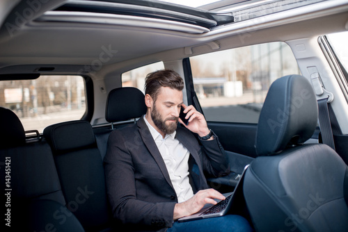 Handsome businessman talking with phone sitting with laptop on the backseat of the car © rh2010