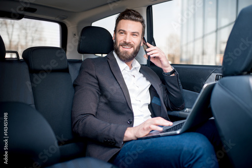 Handsome businessman talking with phone sitting with laptop on the backseat of the car © rh2010