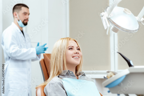 Ready for the checkup. Cheerful young woman smiling happily sitting in a dental chair with her dentist on the background