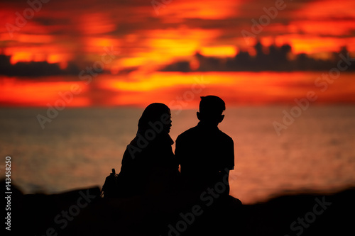 Silhouettes of a young man and a girl sitting on the beach at sunset time