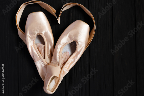 Ballet pointe shoes on black wooden background with ribbons in shape of a heart