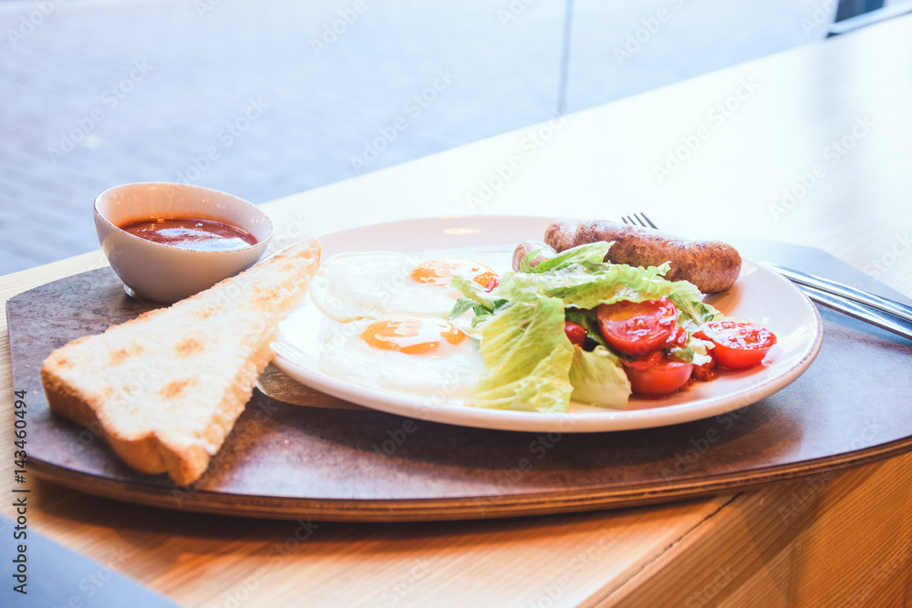 Fried eggs with appetizing sausages, toast bread and fresh salad.