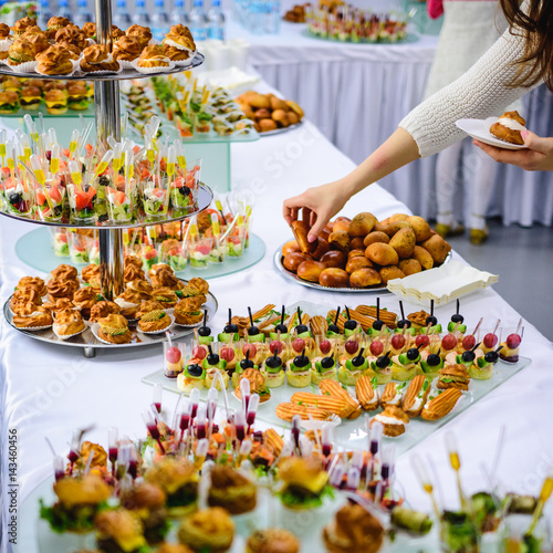 Beautifully decorated catering banquet table with burgers, profiteroles, salads and cold snacks. Variety of tasty delicious snacks on the table