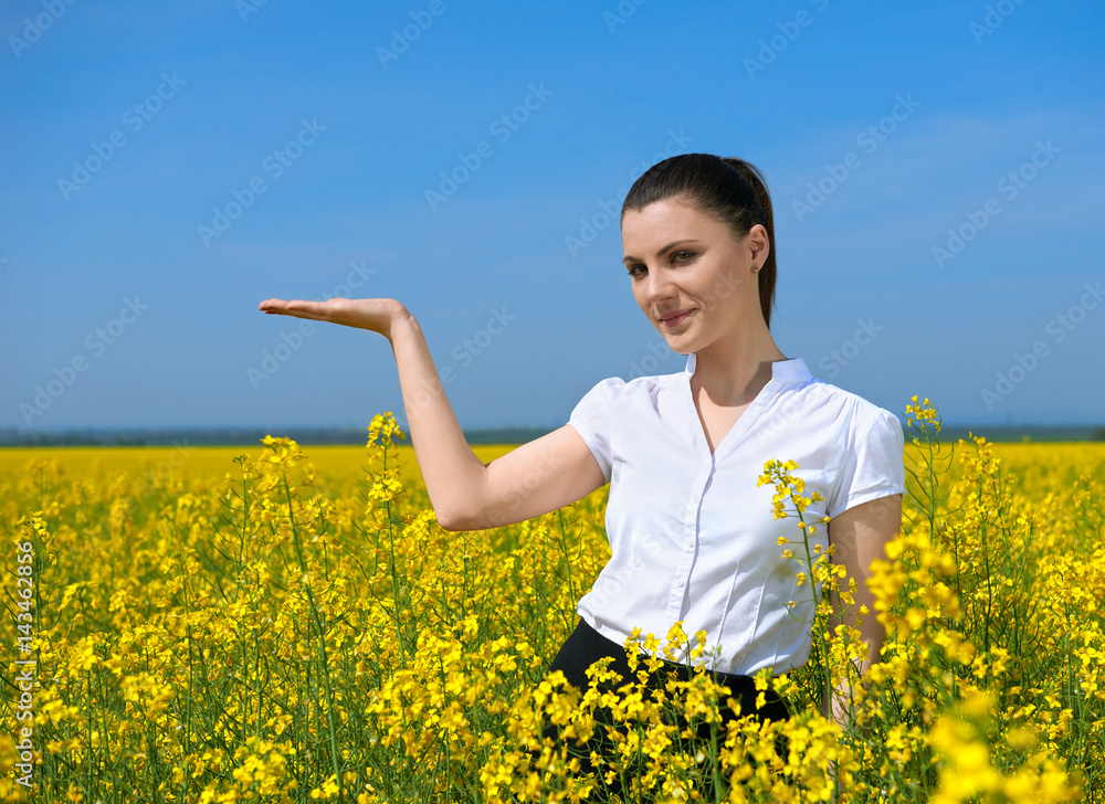 Girl in yellow flower field. Show palm. Hold in palm of something and smile. Beautiful spring landscape, bright sunny day, rapeseed Girl in yellow flower field. Show palm. Hold in palm of something and smile. Beautiful spring landscape, bright sunny day, rapeseed