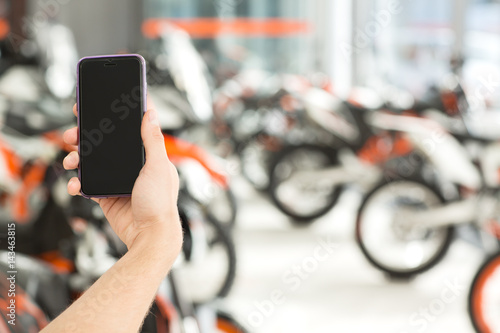 Online banking. Cropped closeup of a hand holding a smartphone with a copyspace on the screen motorcycle salon on the background