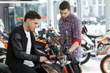 Quality guaranteed. Young male motorcycle salon manager showing his cheerful customer a new motorbike for sale