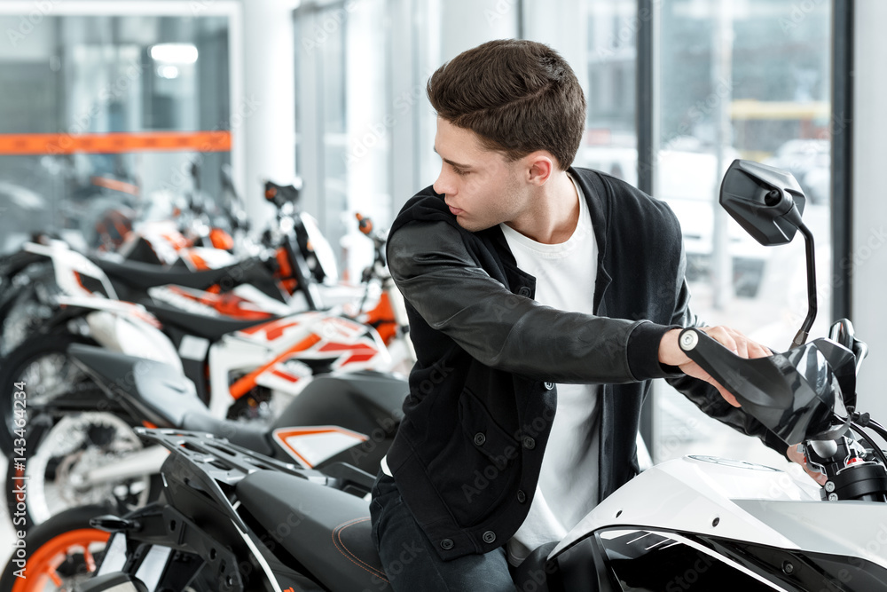 Ready for road trips. Young male customer sitting on a new motorbike looking over his shoulder at the motorcycle salon Ready for road trips. Young male customer sitting on a new motorbike looking over his shoulder at the motorcycle salon