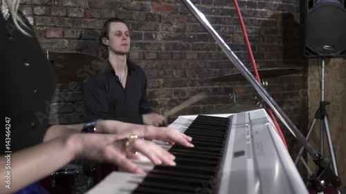Closeup of woman's handsplaying the synthesiser with man playing the drums on the background