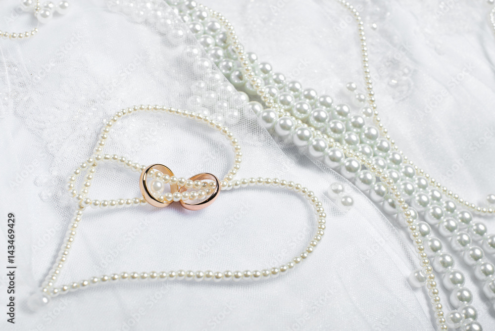 Gold wedding rings lie on a wedding dress. Against the background of the necklace of pearls Gold wedding rings lie on a wedding dress. Against the background of the necklace of pearls
