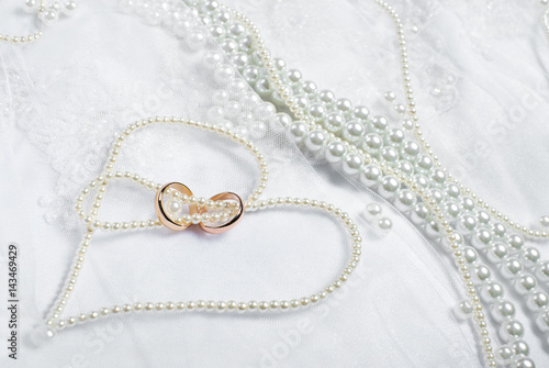 Gold wedding rings lie on a wedding dress. Against the background of the necklace of pearls 