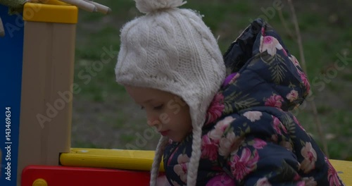 Six Year Old Blonde Girl is Playing in a Park Zone Dressed in a Colored Waiscoat, Knitted Hat With Balabon, Pink Pants, in Autumn in Poland photo