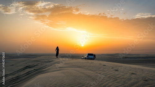 Frau mit Geländewagen auf einer Düne in der Wüste von Katar bei Sonnenuntergang photo