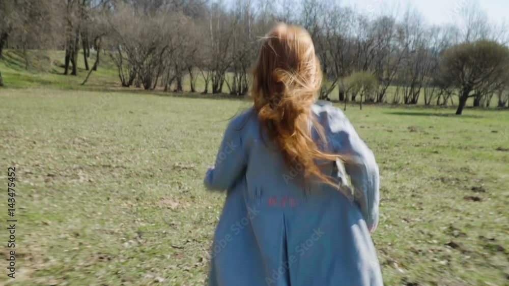 Redhead girl is running across the field in the spring park, her hair fluttering in the wind, steadicam shot Redhead girl is running across the field in the spring park, her hair fluttering in the wind, steadicam shot