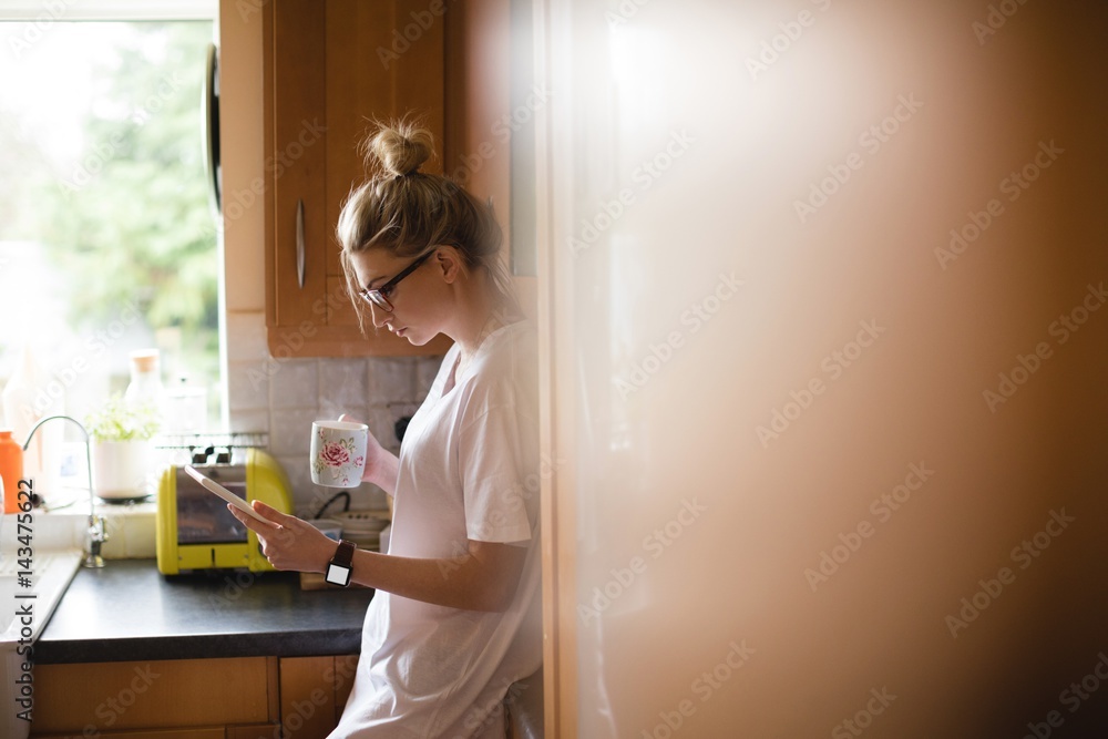 Woman using digital tablet while having coffee in kitchen Woman using digital tablet while having coffee in kitchen